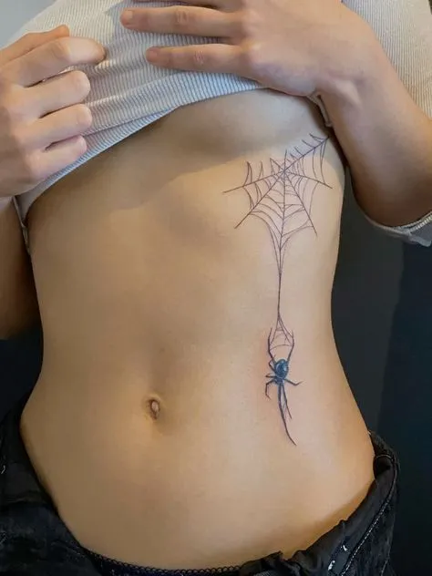 Tatouage d'une araignée descendant de sa toile sous la poitrine d'une jeune femme
