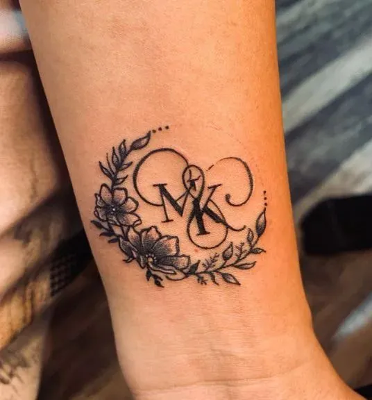 Tatouage de lettres M et K avec des fleurs sur le bras