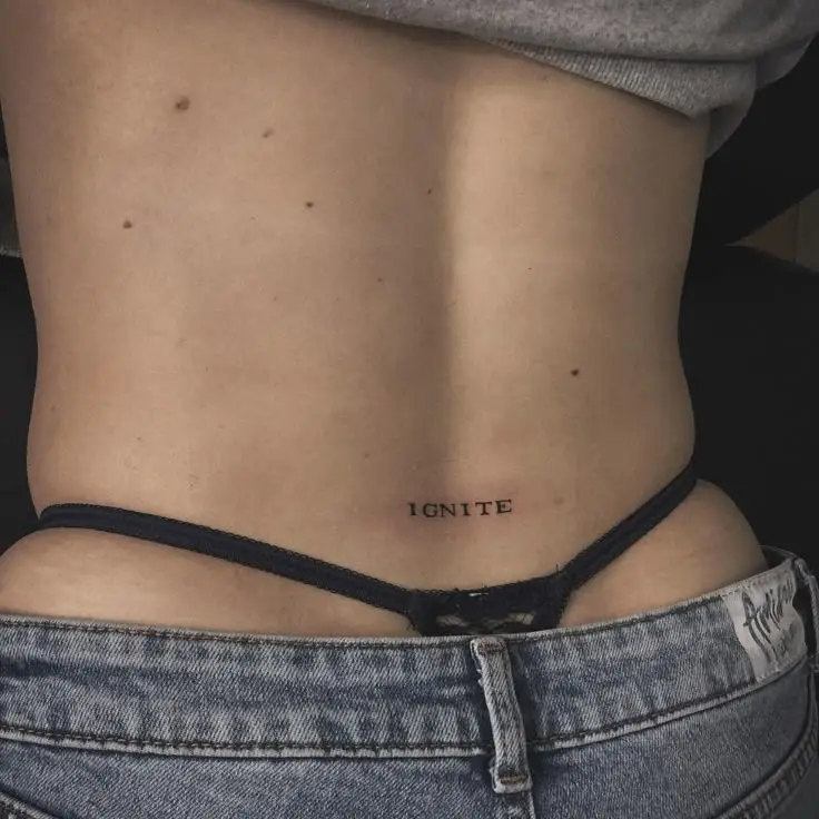 Tatouage de lettres composant le mot ignite dans le bas du dos d'une femme