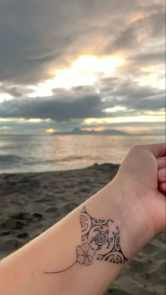Tatouage d'une raie manta sur le bras d'un homme, avec la mer dans le fond 