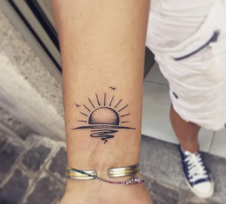Tatouage d'un soleil minimaliste avec la mer, sur l'avant bras d'une femme