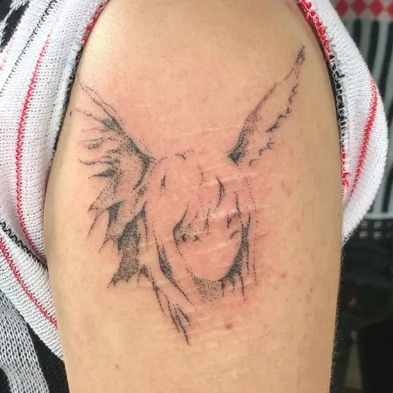 Tatouage recouvrant une cicatrice, formant un visage, sur l'épaule d'une femme