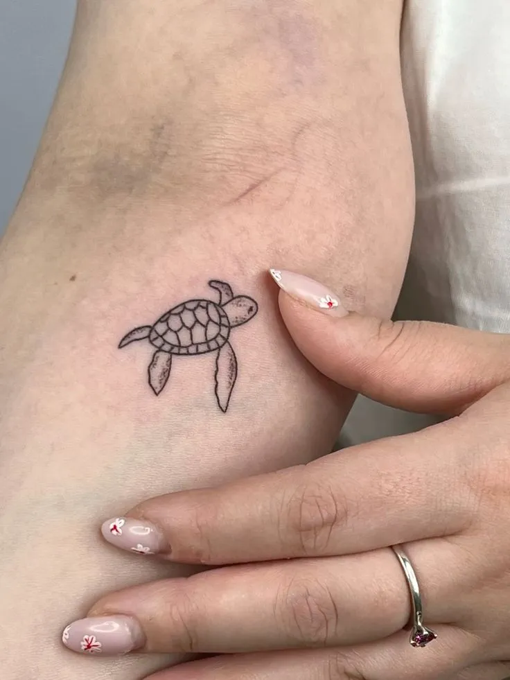 Tatouage tortue minimaliste sur le bras d'une femme