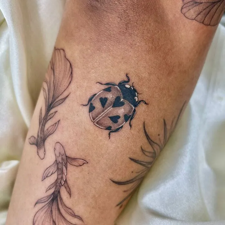 Tatouage coccinelle avec des cœurs sur le bras d'un homme