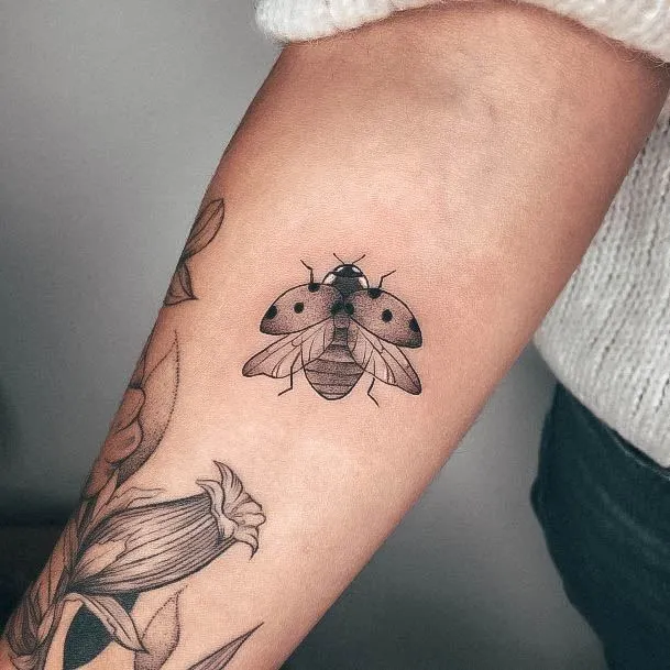 Tatouage coccinelle prenant son envol sur le bras d'une femme
